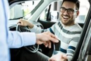Young happy man receiving new car keys in a showroom. Happy man receiving keys for his new car in a showroom.