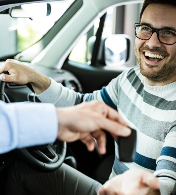 Happy man receiving keys for his new car in a showroom.